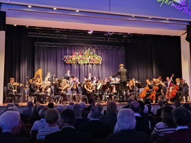 Sinfonieorchester auf einer Bühne. Im Vordergrund Menschen, die auf die Bühne sehen.