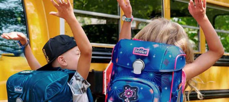 das foto zeigt einen schüler und eine schülerin vor einem Schulbus jubelnd.